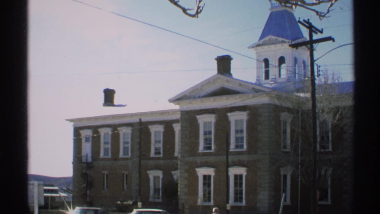 Stone courthouse with blue cupola, white trim, power lines, trees, and parked cars.