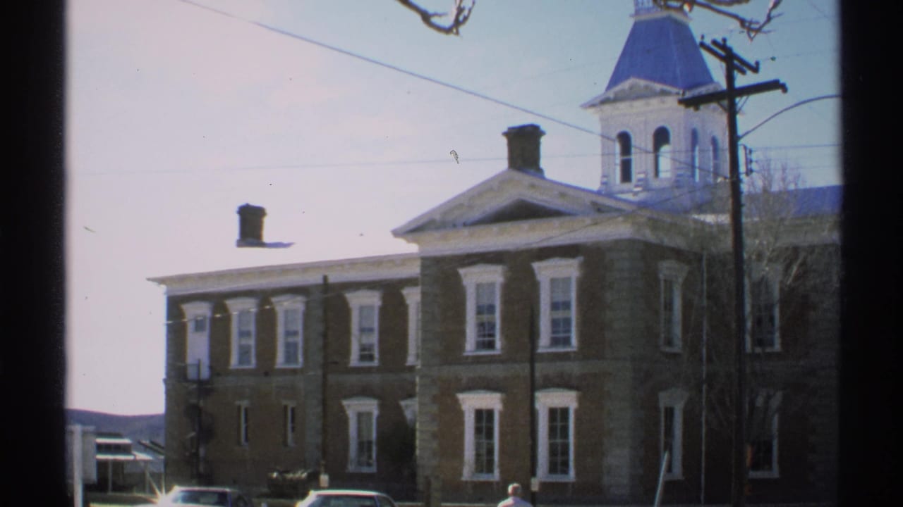 Courthouse exterior with cupola, power pole, overhead wires, trees, and cars.