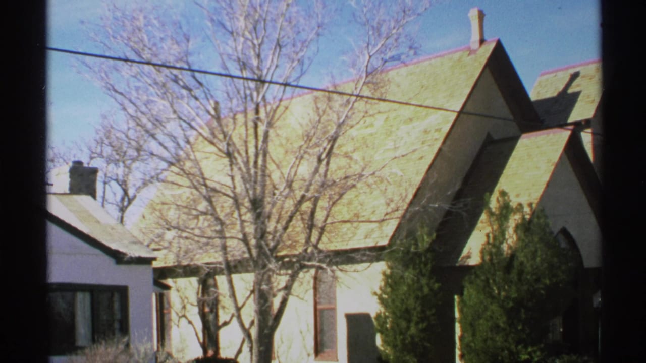 Church roof and steeple beside bare trees, power lines, shrubs, and a neighboring house.