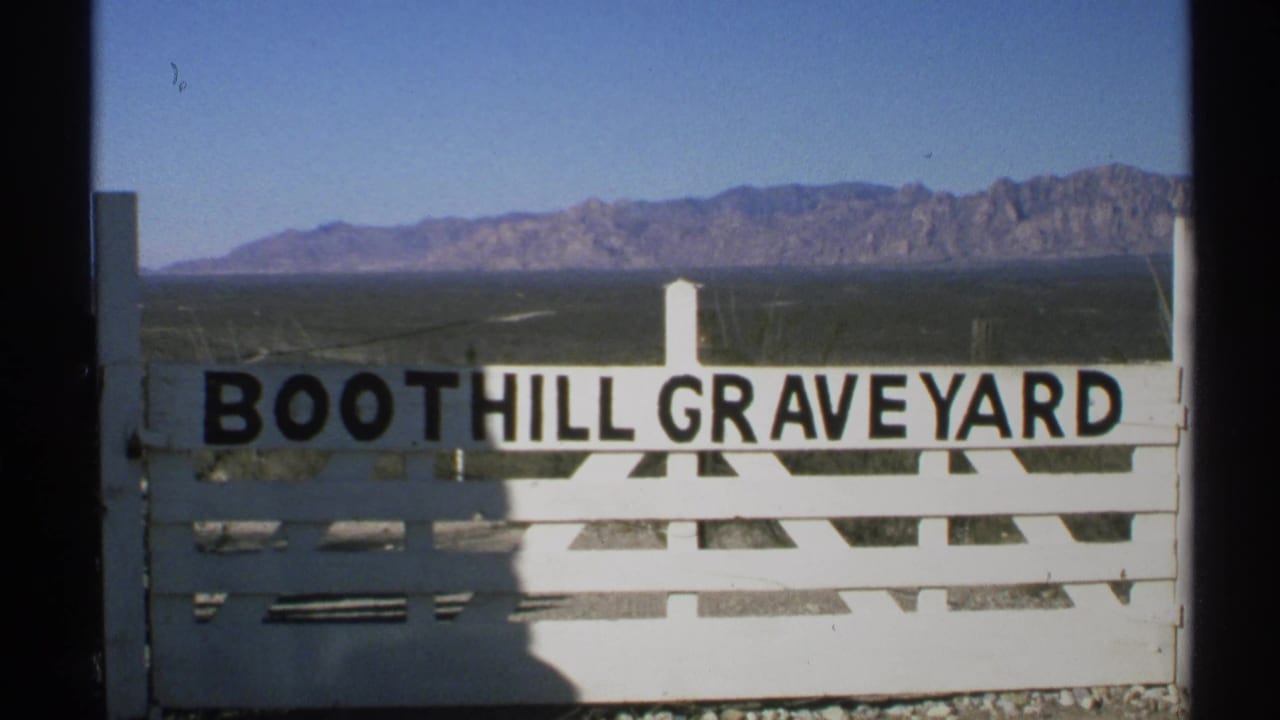 1972 Arizona 8mm frame showing a white Boothill Graveyard entrance sign with rugged mountains in the distance.