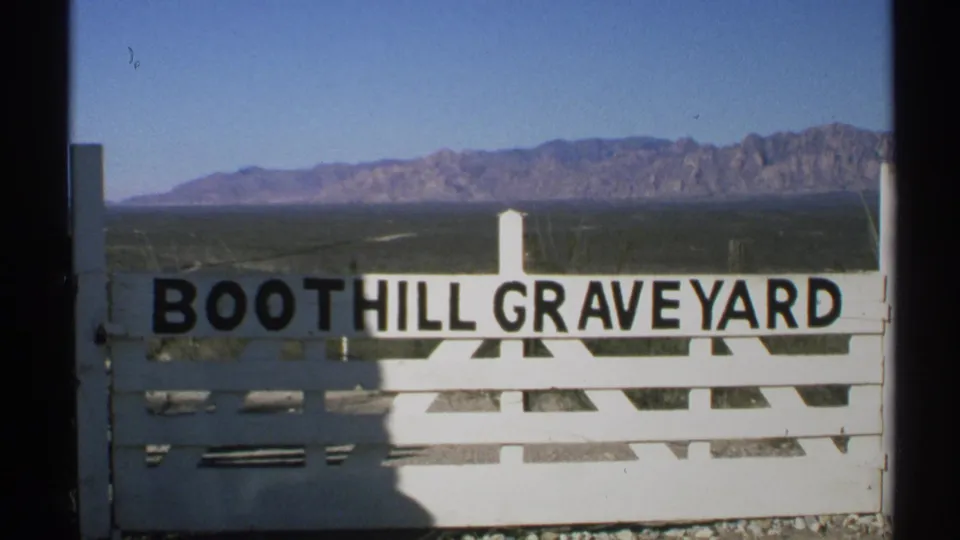 1972 Arizona 8mm frame showing a white Boothill Graveyard entrance sign with rugged mountains in the distance.