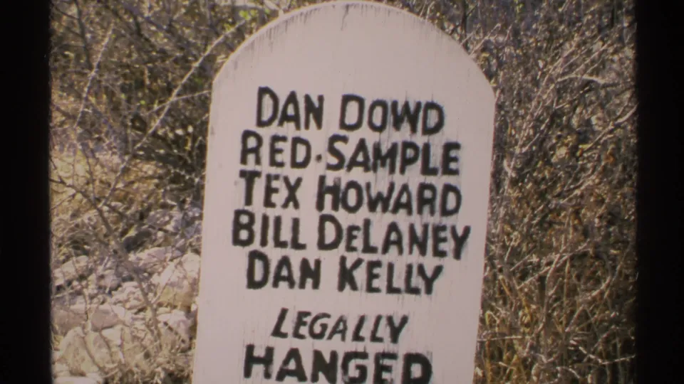 Close 1972 Arizona frame of the hand-painted Legally Hanged marker, surrounded by dry brush and pale stones.