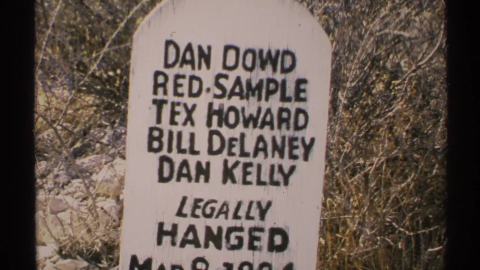 Final 8mm frame of the Arizona marker, showing black lettering on white paint against dry brush and rocks.