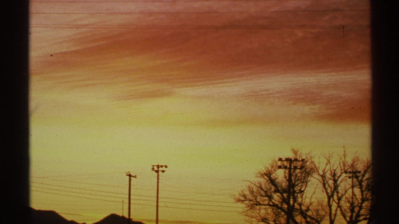 Orange and yellow sunset sky above silhouetted utility poles, wires, bare trees, and low rooflines.
