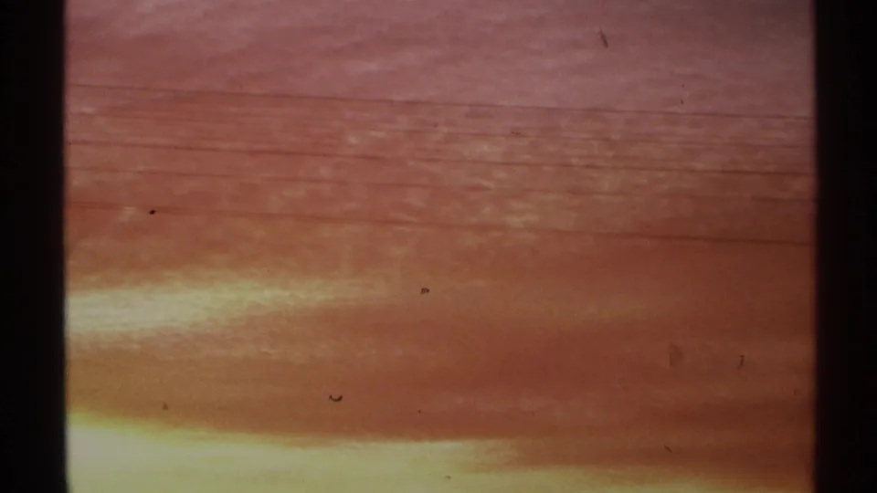 1972 Arizona 8mm frame showing a hazy orange sunset sky, dark film-edge shadows, and a low yellow glow near the horizon.