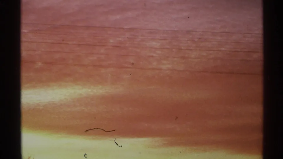 1972 Arizona 8mm frame with warm orange cloud bands, small film marks, and dark vertical shadows at the edges of the frame.