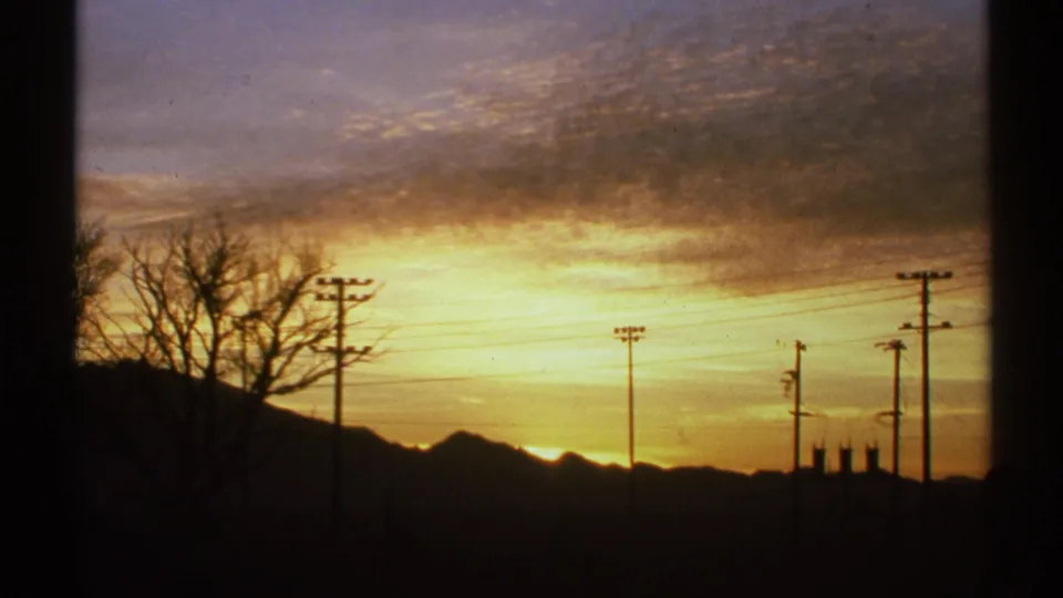 1972 Arizona 8mm frame with distant mountains, utility poles, overhead wires, and a warm sunset sky.