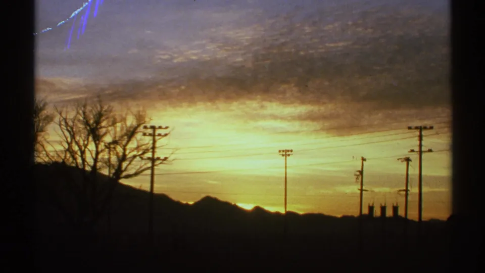Arizona sunrise scene with low mountains, utility poles, silhouetted tree branches, and visible 8mm frame-edge artifacts.