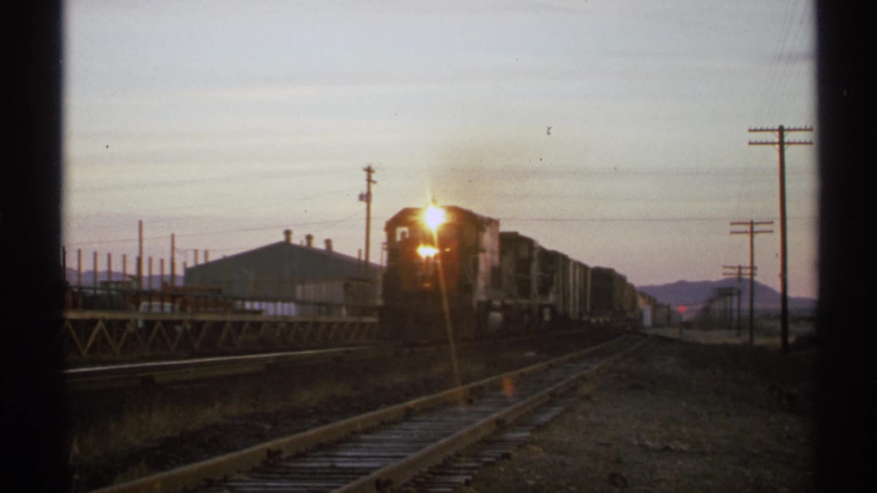 Locomotive headlight flares as the freight train moves closer along the track.