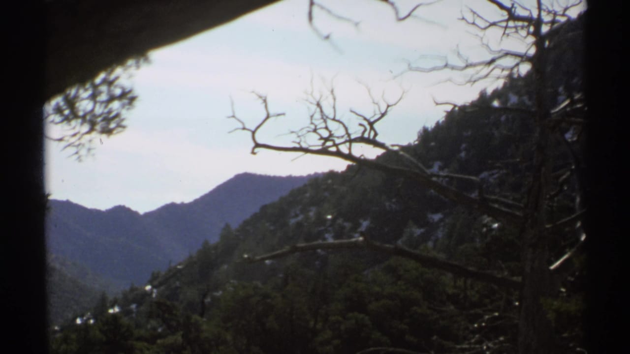 1972 Arizona 8mm frame showing a shaded mountain overlook with bare branches, evergreen slopes, and distant ridges.