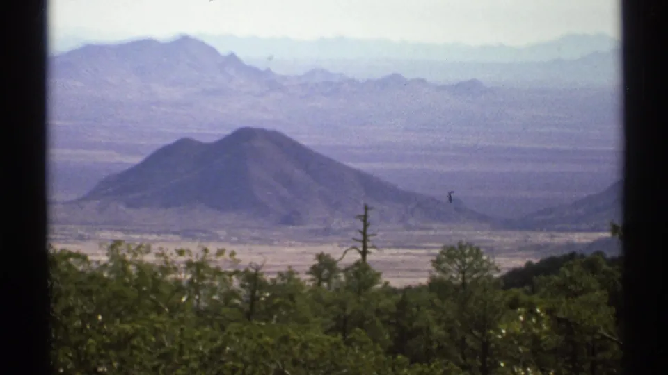 1972 Arizona 8mm panorama showing a rounded desert hill, layered mountains, and trees in the foreground.