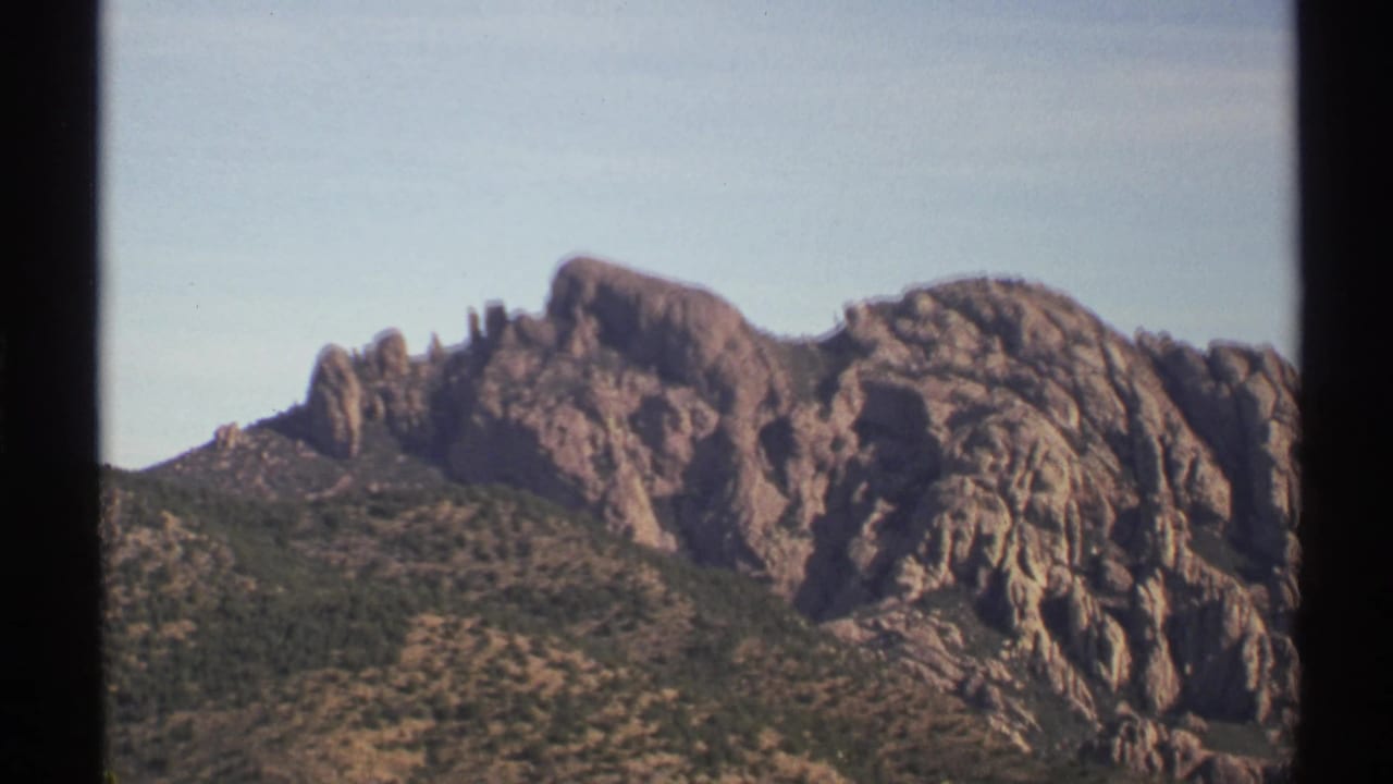 Rocky mountain peaks above scrub-covered desert slopes under a pale blue sky.