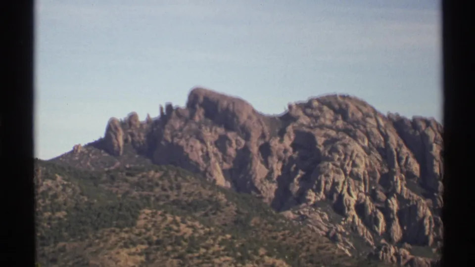 1972 Arizona 8mm frame showing rugged rocky peaks rising above brushy desert slopes in bright daylight.