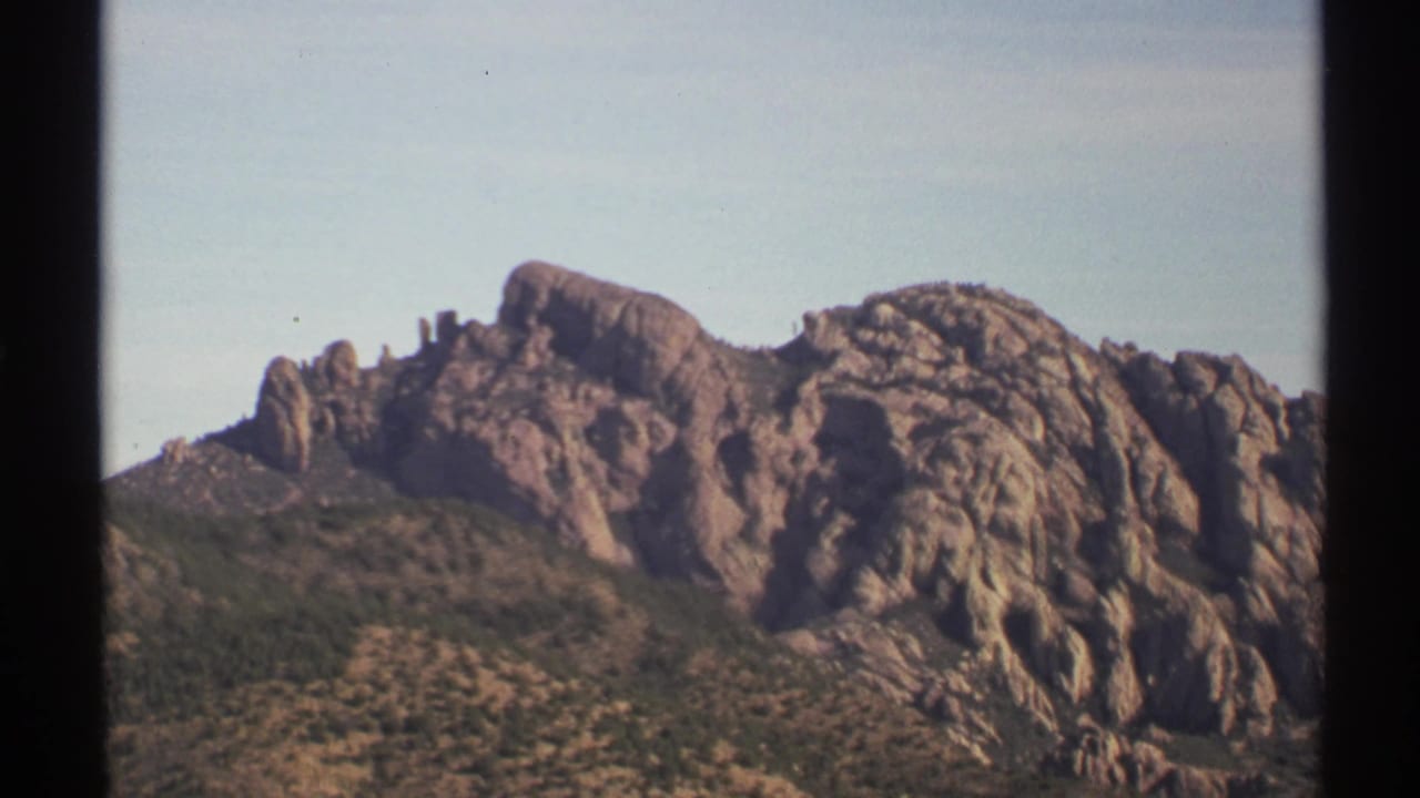 Similar view of jagged rock formations and low desert vegetation beneath clear sky.