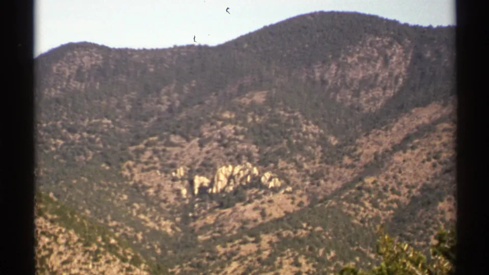 1972 Arizona home-movie frame of a scrub-covered desert ridge with pale rock patches and visible 8mm dust marks.