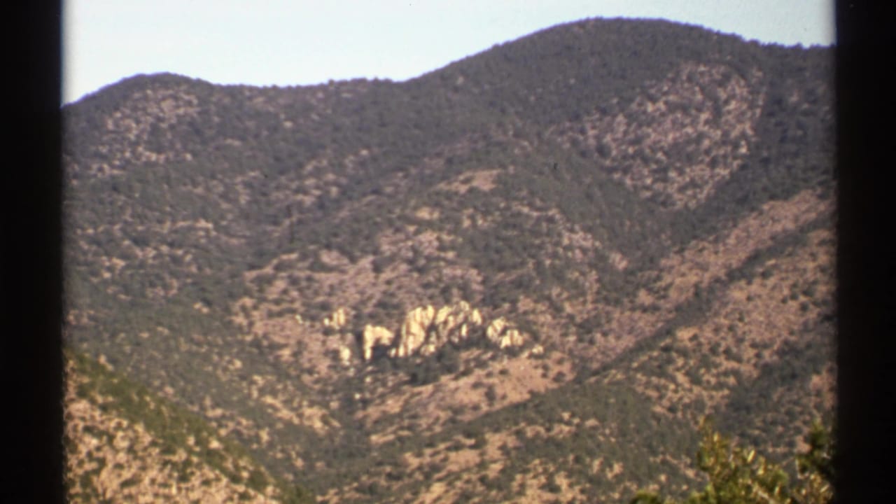 Scrub-covered Arizona ridge with pale rock outcrops and dark film borders.