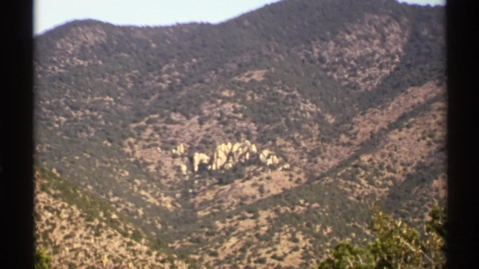 Arizona home-movie frame showing a scrubby mountain slope with pale exposed rock and soft 8mm color.