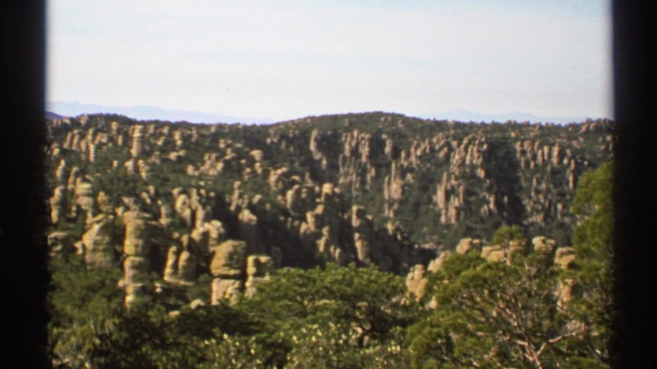 Forested ridge with tall stone pillars under a pale sky.
