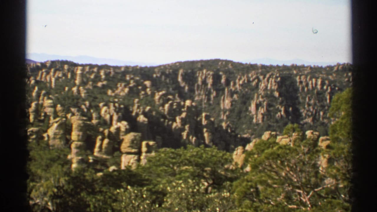 Rock columns across a wooded ridge with distant mountains beyond.