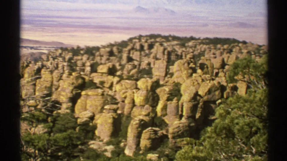 Closer 8mm view of Arizona clustered rock pillars, scrub trees, and a purple-grey sky over distant terrain.