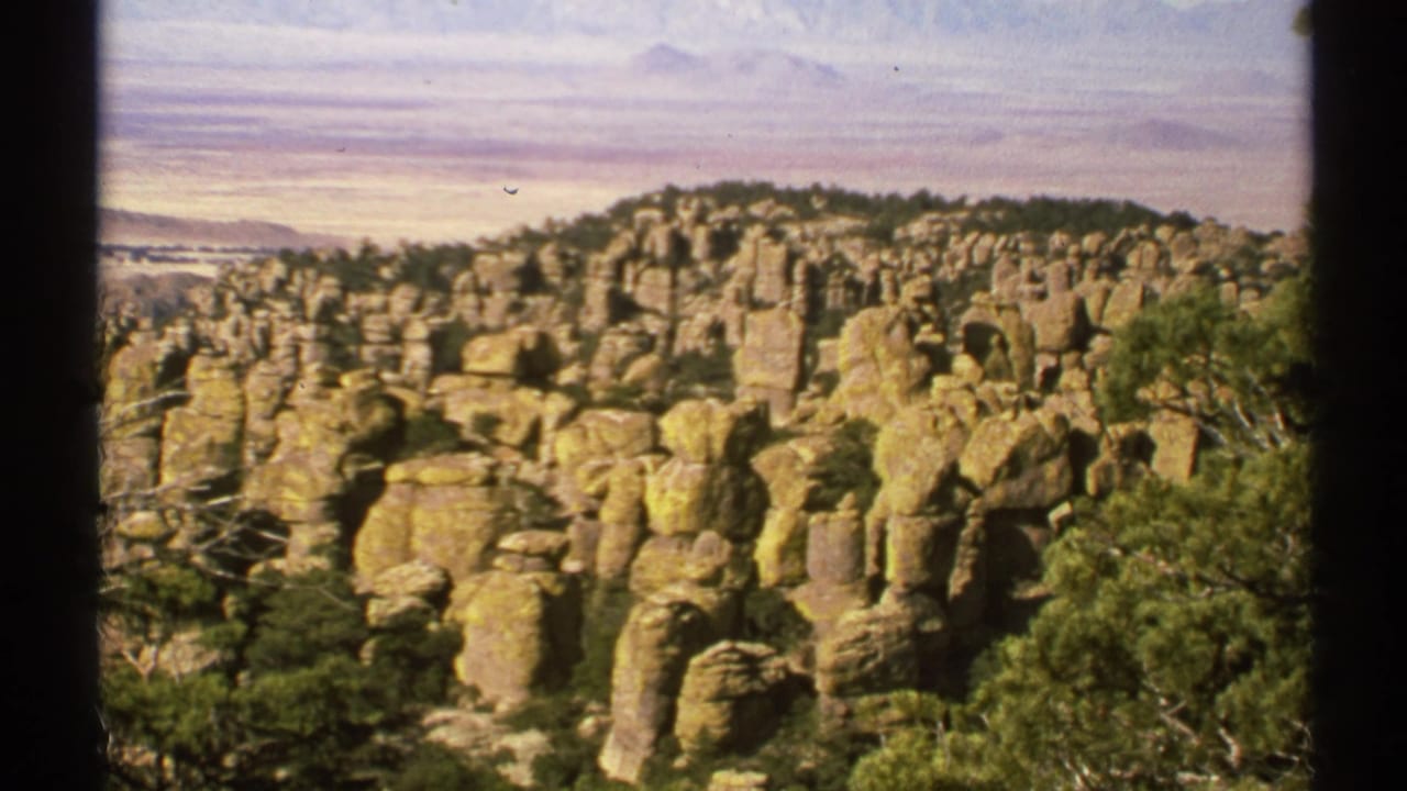 1972 Arizona 8mm view of clustered tan rock formations, scrub trees, and a pale sky from an elevated vantage point.