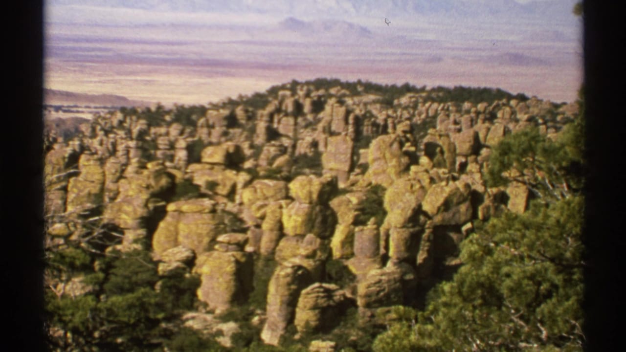 Rugged tan rock spires and green vegetation under a bright sky.