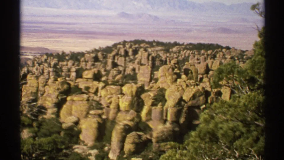 Arizona home-movie frame from 1972 showing dense tan rock columns with green trees and scrub from a scenic overlook.