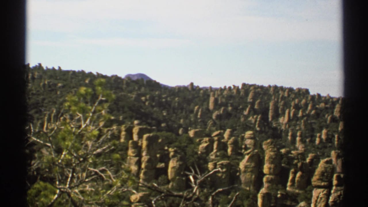Tan rock pillars on a green hillside beneath a pale sky.