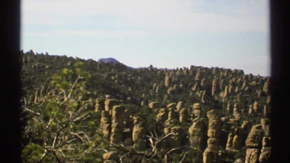 1972 Arizona 8mm frame showing tan rock columns across a tree-covered hillside under bright daylight.