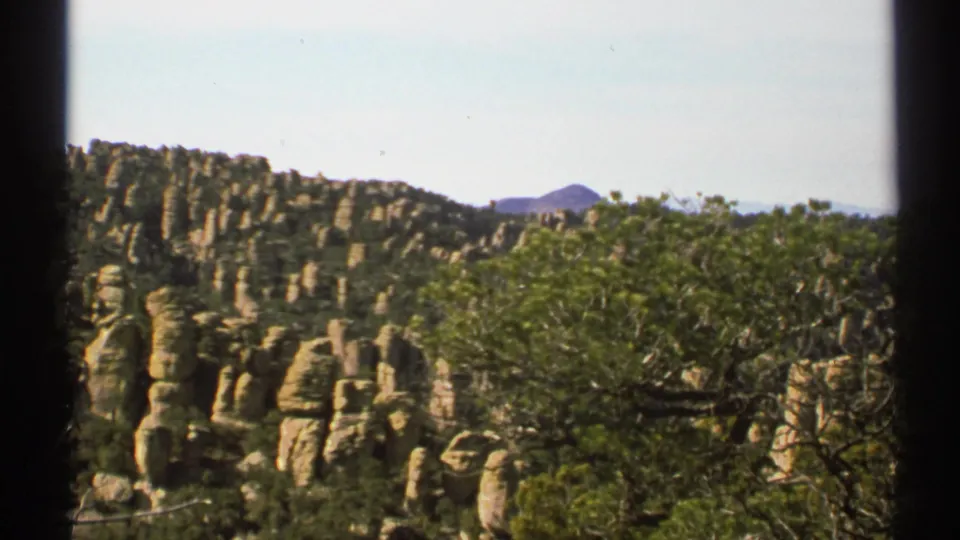 1972 Arizona home-movie frame with foreground trees, tan rock pillars, and a sunlit ridge in the distance.