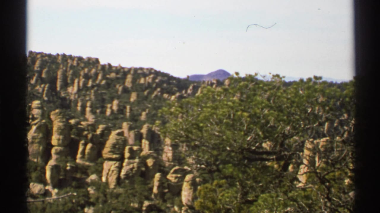 1972 Arizona 8mm frame showing tan rock formations, green trees, distant hills, and dark vertical film borders.