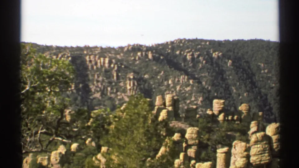 1972 Arizona 8mm view of a wooded hillside broken by pale rock pillars, framed by black film edges.