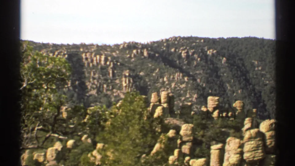 1972 Arizona 8mm frame with leafy foreground trees, tan rock formations, and green ridges in the background.