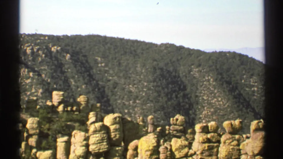 1972 Arizona 8mm view of clustered rock spires, green mountain slopes, and a bright sky near the end of the pan.