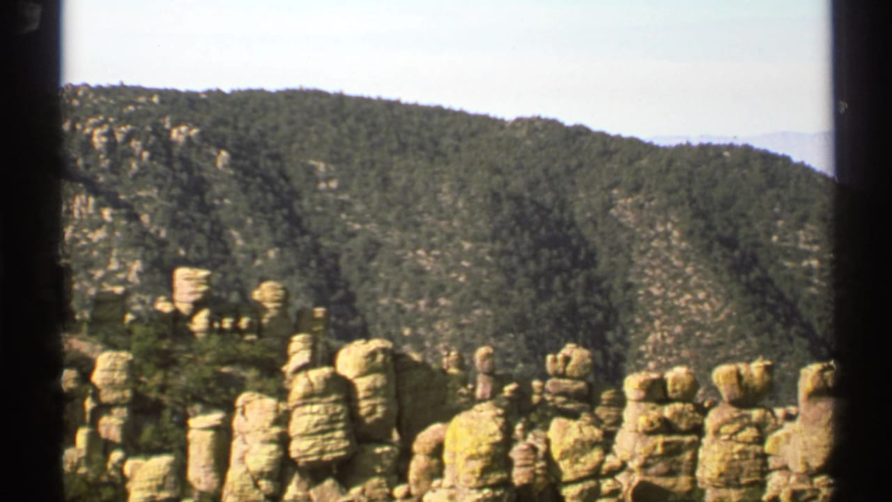 1972 Arizona 8mm frame showing pale rounded rock spires in the foreground and a wooded mountainside behind them.