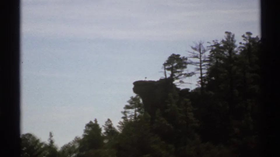 1972 Arizona 8mm frame showing a dark rock ledge and tree silhouettes against a pale, lightly clouded sky.