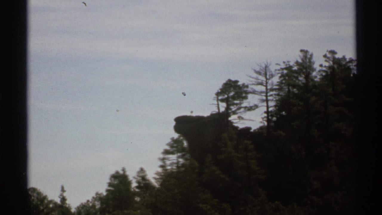 Similar hillside view with trees and a protruding rock formation near the skyline.