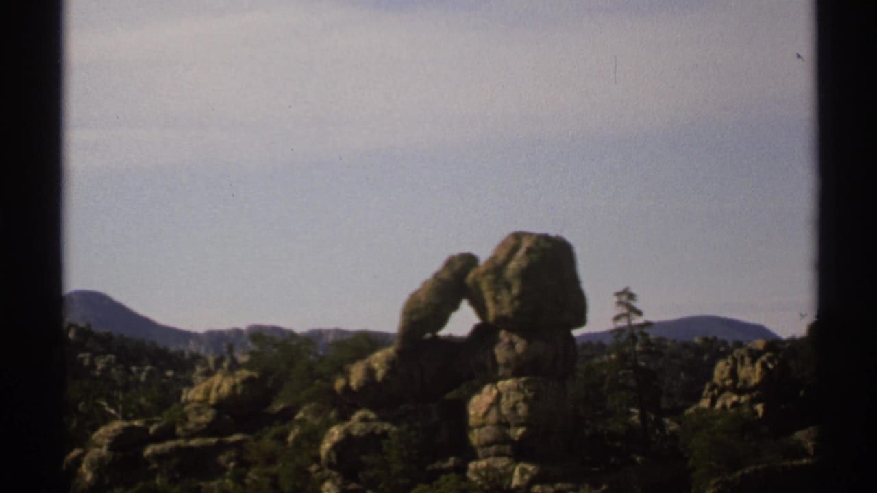 Rock formation framed by dark film edges with trees and distant mountains behind it.