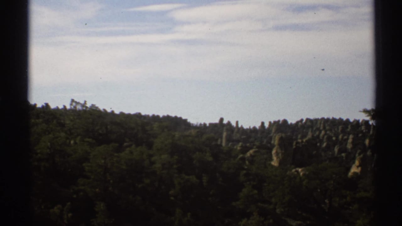 Forested rocky ridge under a pale sky, partly bordered by dark vertical frame edges.