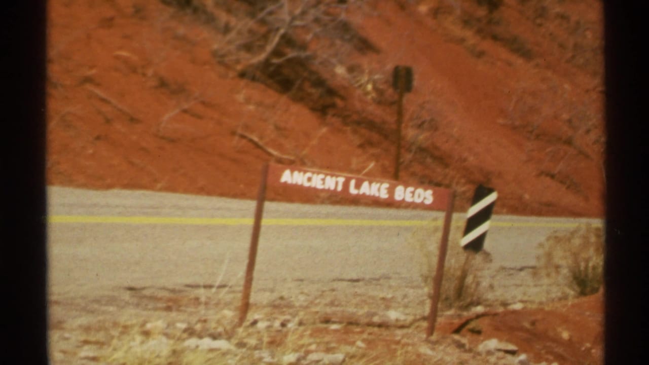 Roadside Ancient Lake Beds sign beside a road and red dirt slope.