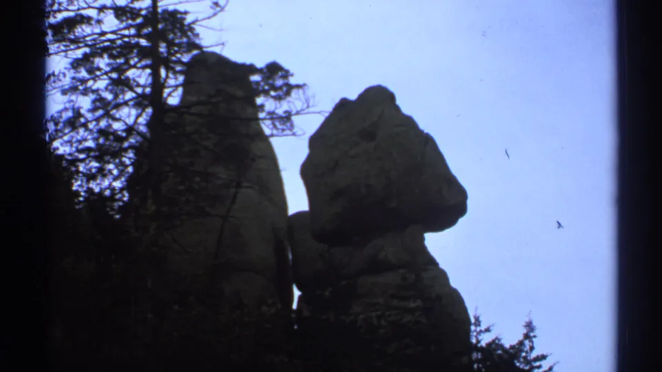 1972 Arizona 8mm low-angle frame of massive weathered boulders, dark tree branches, and a pale blue sky.