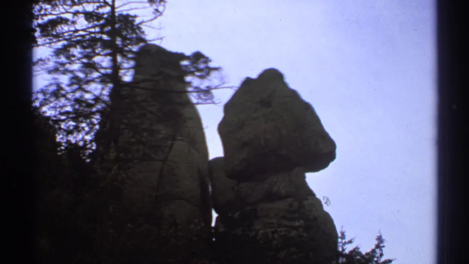 1972 Arizona 8mm view of a weathered stone formation seen in silhouette through nearby trees.