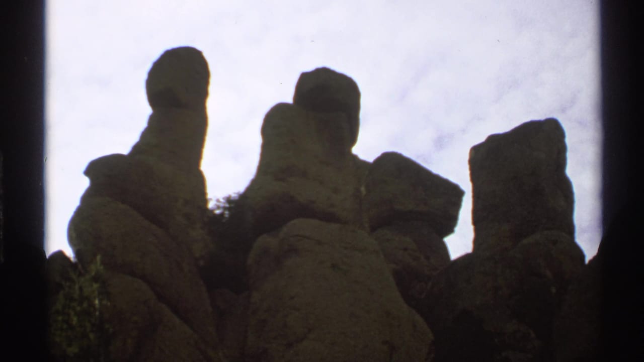 1972 Arizona 8mm frame showing clustered rock formations in silhouette beneath a pale overcast sky.