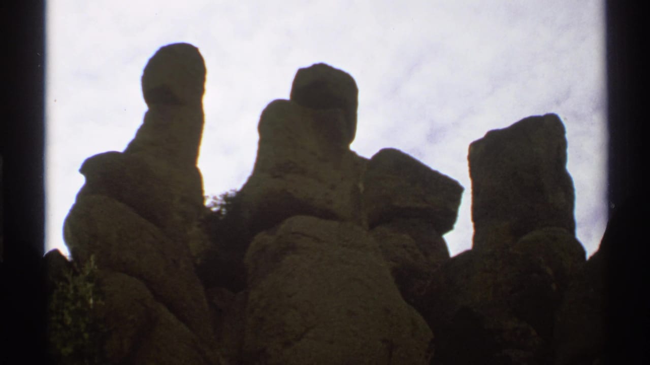Several tall boulders and rock columns silhouetted below a cloudy sky.