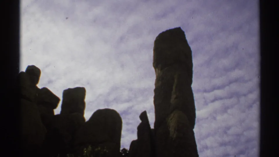 1972 Arizona 8mm frame with a prominent rock pillar and surrounding boulders silhouetted beneath rippled cloud cover.