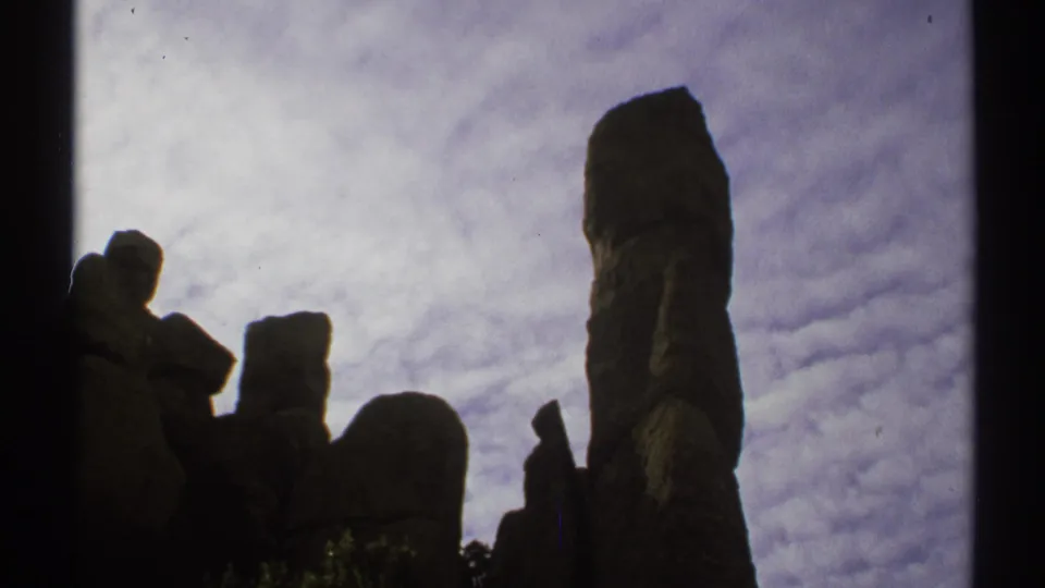 1972 Arizona 8mm frame showing tall rock formations in silhouette beneath a textured cloudy sky.