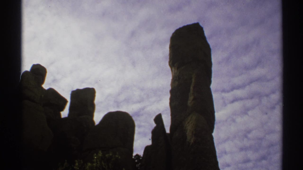 Silhouetted stone columns and a tall spire below a cloudy sky.