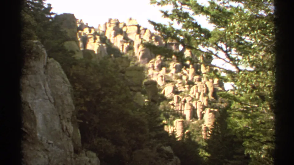 Vintage Arizona frame showing bright stone formations framed by trees and a darker hillside.