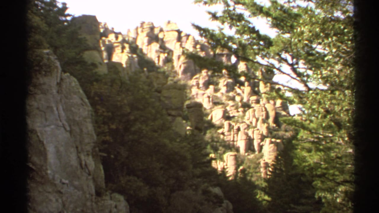 Sunlit rock cliffs and trees seen through dark film-frame borders.