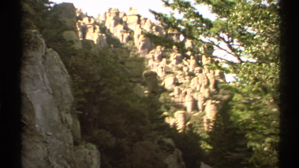 1972 Arizona 8mm frame with sunlit rock formations, wooded slopes, and a dark vertical divider from the film scan.